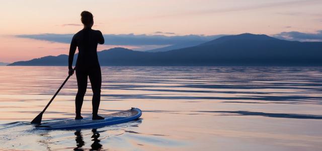 Girl on a paddle board is paddeling during a bright and vibrant sunset
